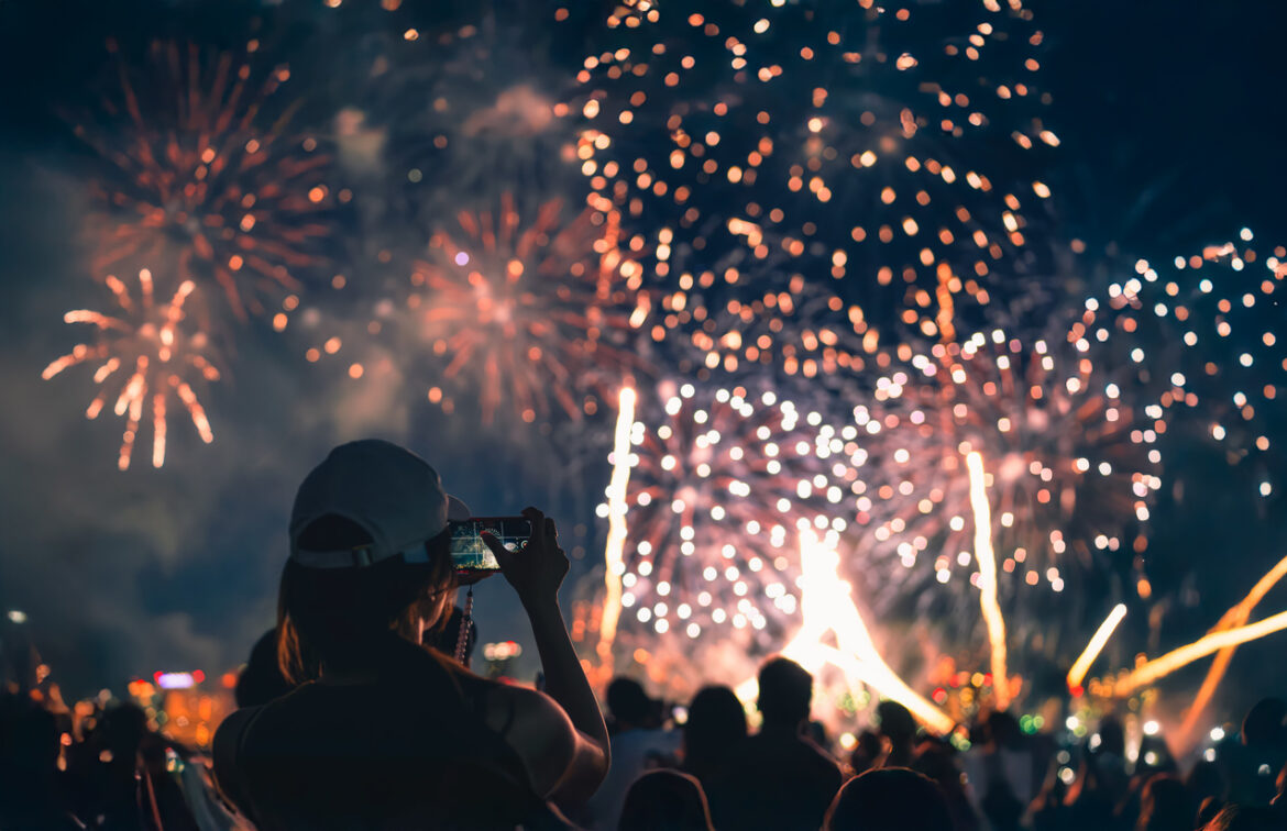 The back of a girl in a baseball cap filming a fireworks display on her mobile phone