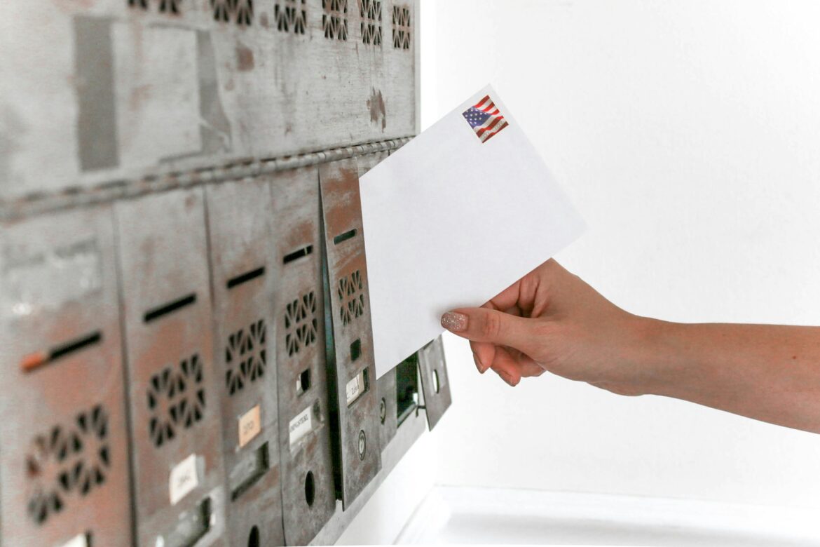 A hand with sparkly nail polish is mailing a ballot in.