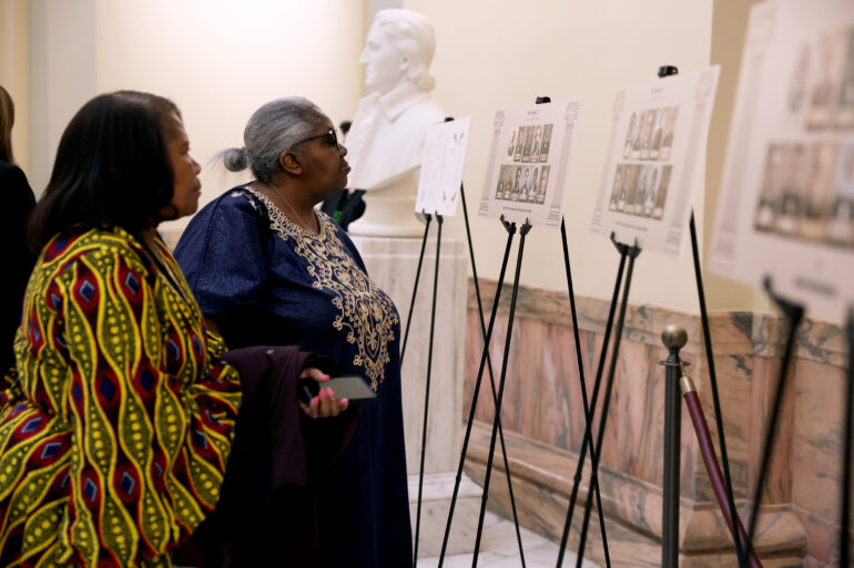 A photo of two Black women looking at a memorial for the Original 33, the first African American members of the Georgia state legislature