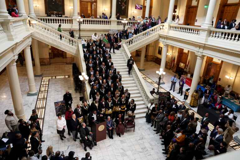 A wide photo of the South Wing steps of the Georgia State Capitol with a large crowd gathered and speakers at the podium.