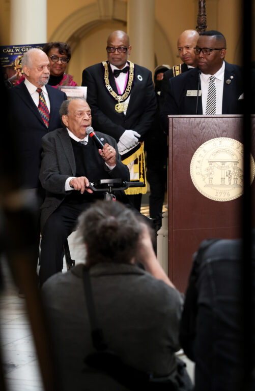 A photo through a crowd of photographers focused on former U.S. Ambassador Andrew Young as he gives a speech