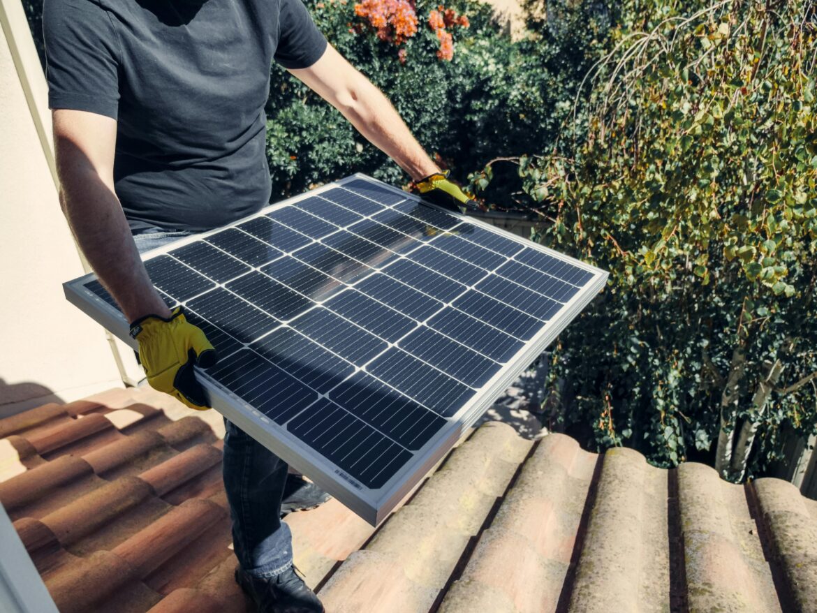 A man carries a solar panel on a roof.