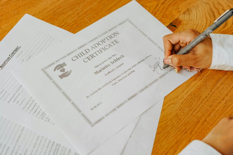 A close up photo of someone signing a child adoption certificate