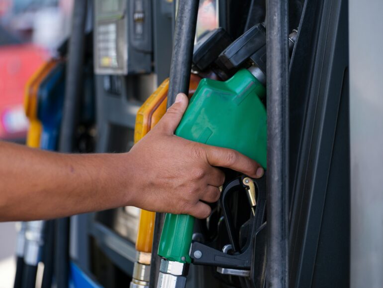 A hand reaches for a gas pump at a gas station.
