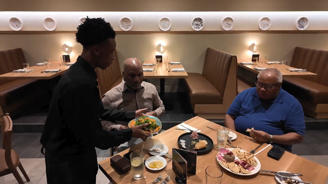 A young man serving a table of two at a restaurant