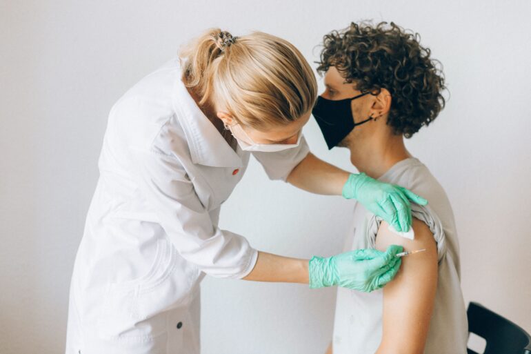 A woman who is dressed like a doctor giving a patient a shot in the shoulder.