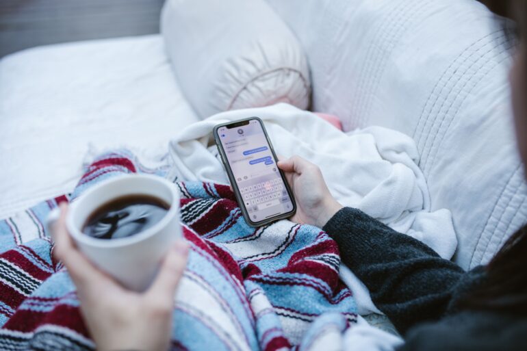 Someone holding a coffee and texting while sitting on a couch