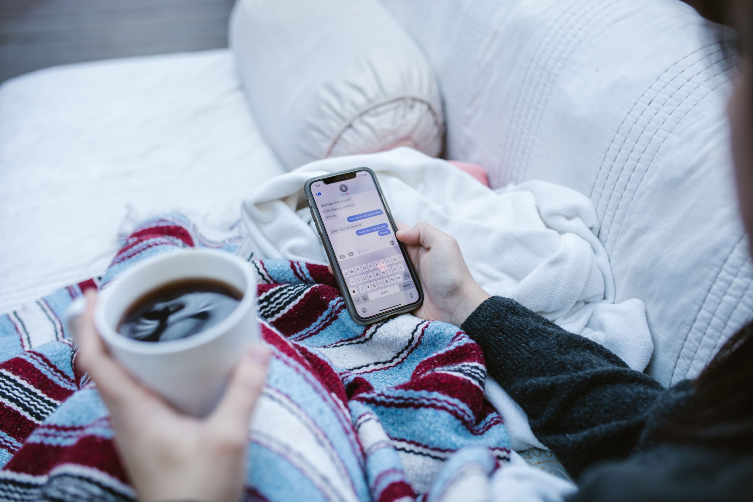 Someone holding a coffee and texting while sitting on a couch